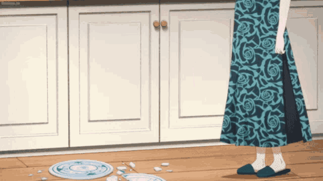 a woman in a blue floral dress stands in front of a broken plate on the floor