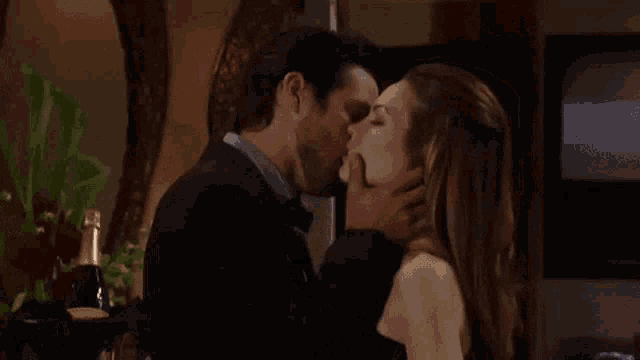 a man and a woman are kissing in a room with a bottle of champagne .
