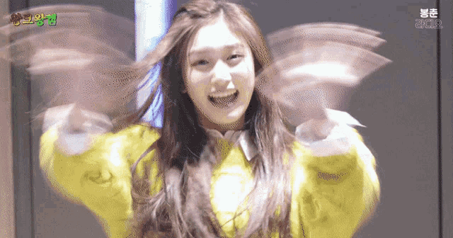 a girl in a yellow sweater has her arms outstretched in front of her face