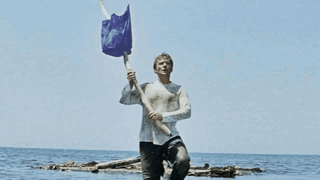 a man is holding a blue flag on a stick in the ocean .