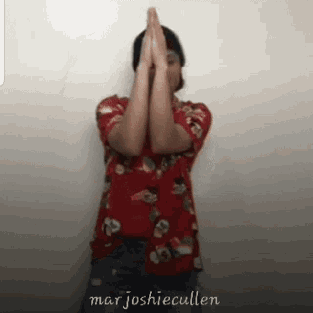 a man in a red shirt holds his hands together in front of his face