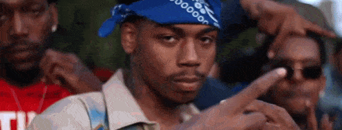 a man wearing a blue bandana is pointing at the camera while standing in front of a crowd of people .
