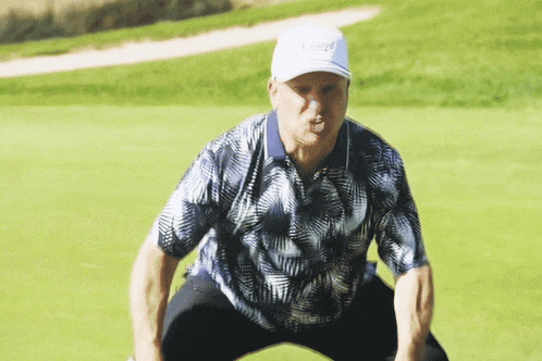 a man squatting on a golf course wearing a hat that says ' kings ' on it