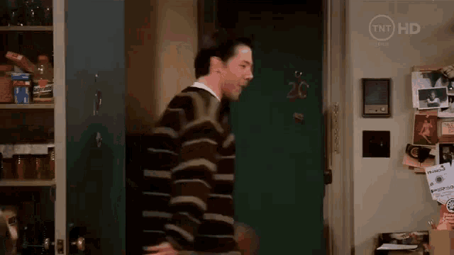 a man in a striped sweater is standing in front of a green door in a kitchen .