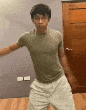 a young man in a green shirt and white shorts is dancing in front of a door .