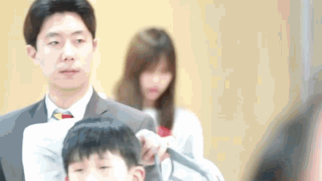 a man in a suit and tie is cutting a boy 's hair .
