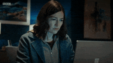 a woman is sitting at a desk with a bbc logo on the bottom left