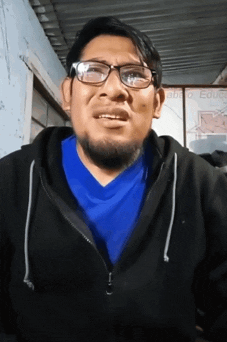 a man wearing glasses and a blue shirt is standing in front of a sign that says " educa "