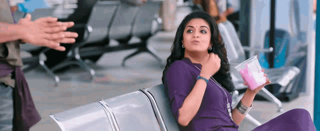 a woman in a purple dress is sitting on a bench holding a cup .