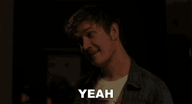 a man in a denim jacket says " yeah " in a dark room