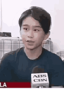 a young boy is talking into a microphone while wearing a black shirt .