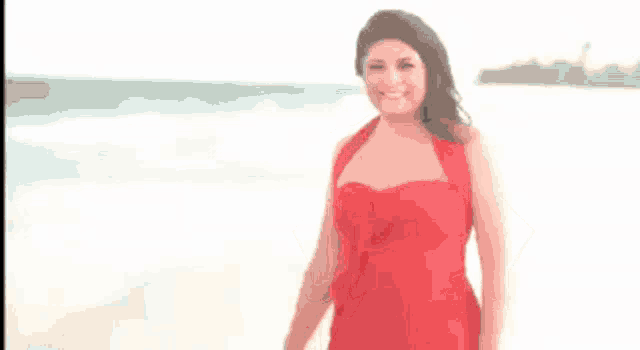 a woman in a red dress is standing on the beach with her hands on her hips