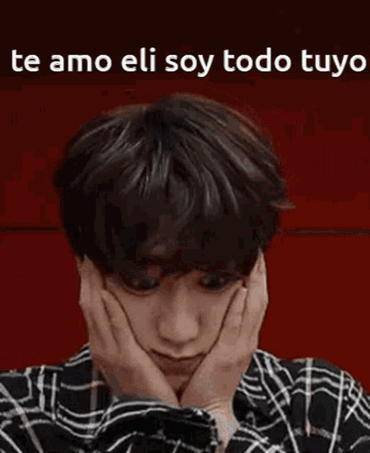 a man in a plaid shirt is covering his face with his hands and says `` te amo eli soy todo tuya '' .