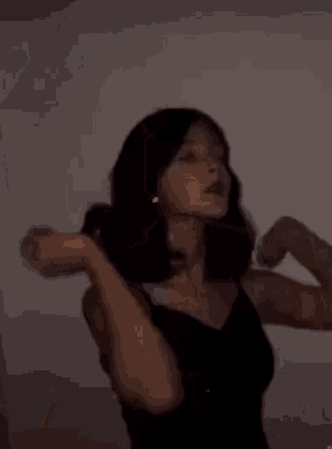 a woman in a black tank top is standing in front of a wall .
