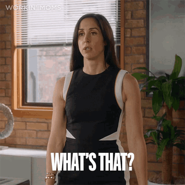 a woman in a black and white dress is standing in front of a window and says " what 's that "