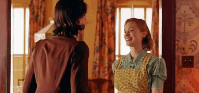two women are standing next to each other in a room talking to each other .