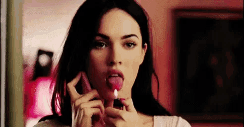 a woman is sticking out her tongue while applying lipstick .