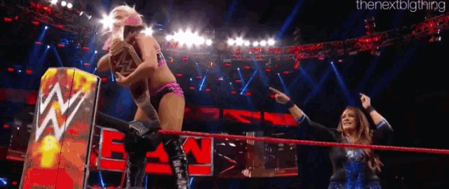 a woman is wrestling another woman in a wrestling ring while a man watches .