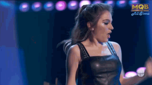 a woman in a leather dress is dancing on a stage in front of a mqb logo