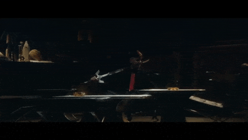 a man in a black suit and red tie is playing a piano