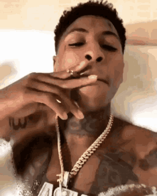 a man is smoking a cigarette while wearing a gold chain .