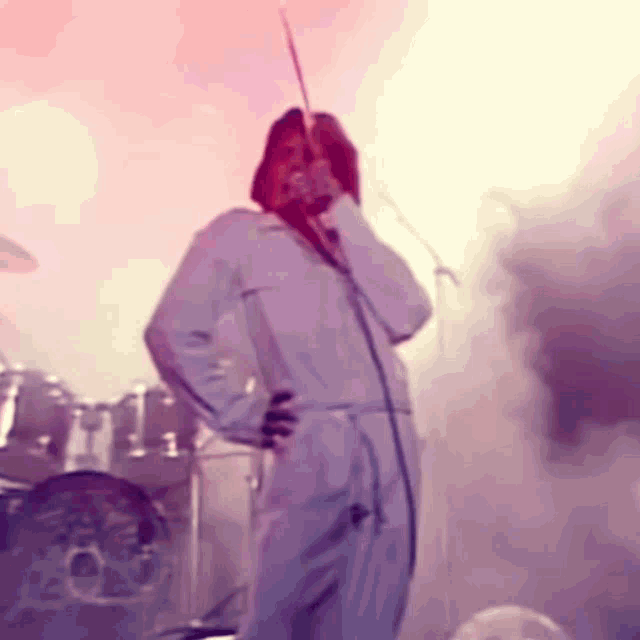 a man in a white jumpsuit sings into a microphone