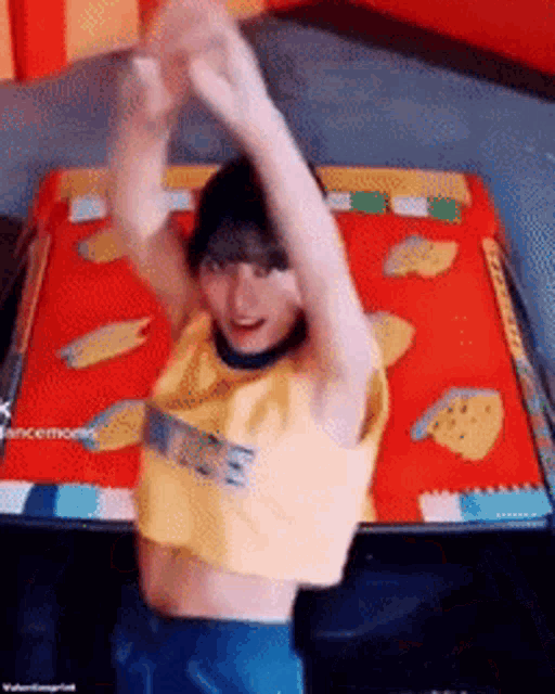 a woman in a yellow crop top is standing in front of a red table with her hands in the air .