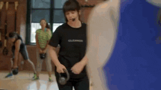a woman is holding a kettlebell in a gym while a group of people are doing exercises .