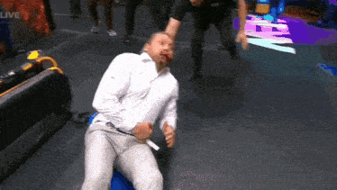 a man in a white shirt is laying on the floor with blood on his face while a referee stands behind him .