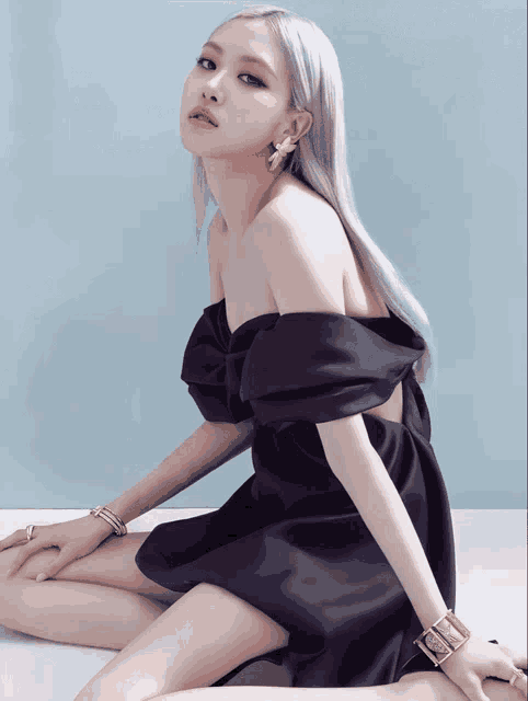 a woman in a black off the shoulder dress is sitting on the floor
