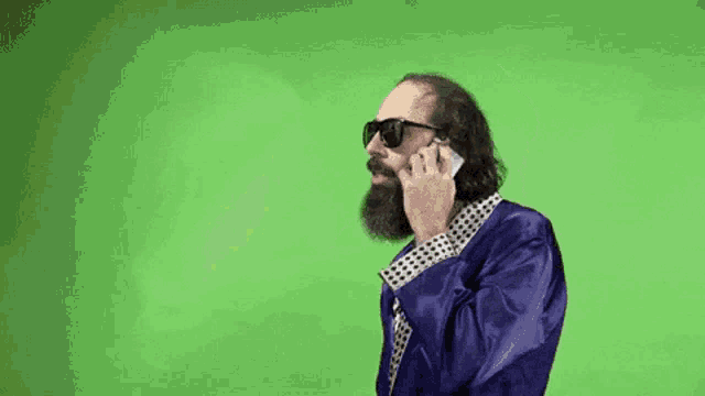 a man with a beard is talking on a cell phone while wearing sunglasses .