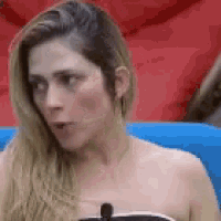 a woman without a shirt is sitting on a blue couch with a microphone in her mouth .