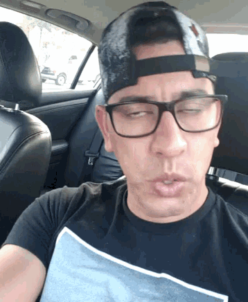 a man wearing glasses and a baseball cap is in a car