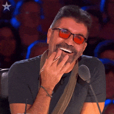 a man wearing red glasses and a scarf is laughing in front of a microphone