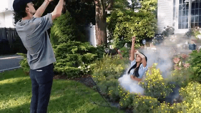 a man is taking a picture of a woman in a garden with smoke coming out of it .