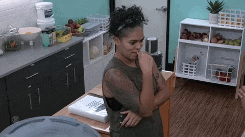 a woman is standing in a kitchen with her hands folded and looking at the camera .