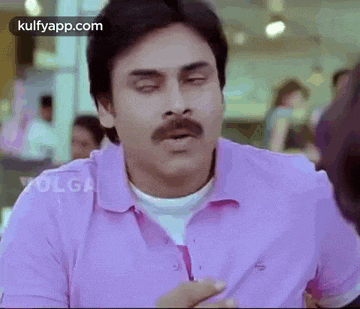 a man with a mustache is wearing a pink shirt and making a face .