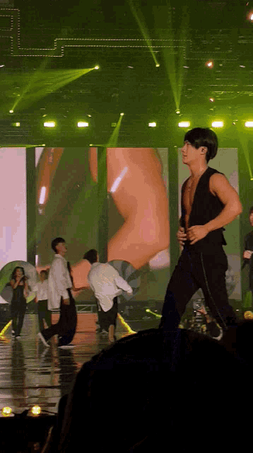 a man in a black vest is dancing on stage