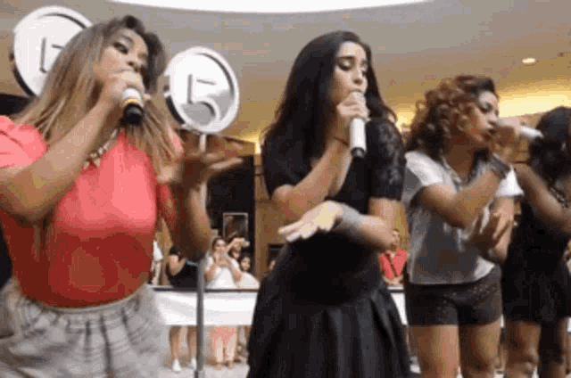 a group of women singing into microphones in front of a sign that has the number 15 on it
