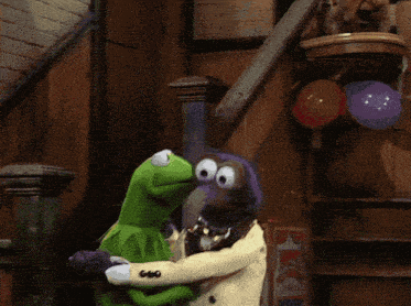 a kermit the frog and a muppet standing next to each other with balloons in the background