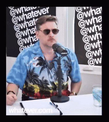 a man wearing sunglasses and a blue shirt is sitting in front of a microphone in front of a sign that says whatever