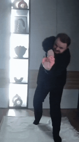 a man in a black shirt is standing in front of a shelf with vases on it
