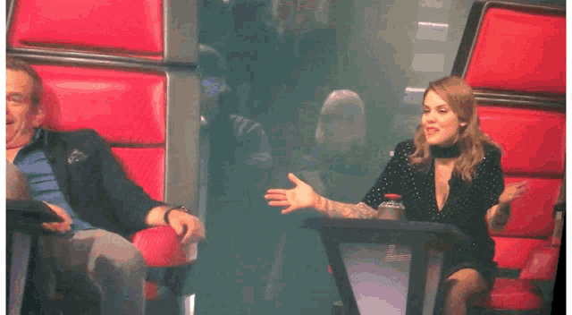 a woman in a black dress is dancing in front of a man sitting in a red chair