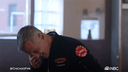 a man in a chicago fire corps uniform wipes his nose with his hand