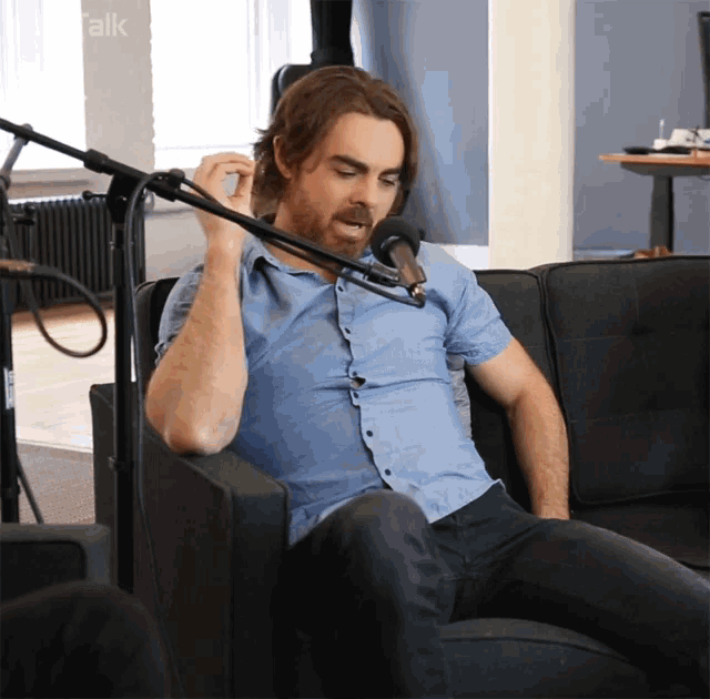 a man in a blue shirt is sitting in front of a microphone with the word talk on the bottom