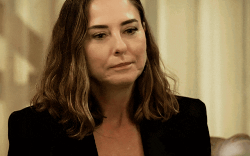 a woman in a black jacket is looking at the camera with a sad look on her face