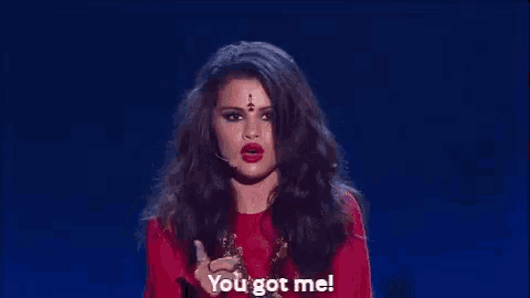 a woman in a red dress is pointing at the camera and saying `` you got me ! ''