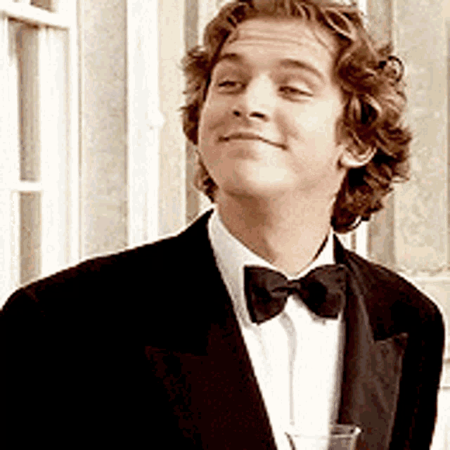 a man in a tuxedo with a bow tie is holding a glass