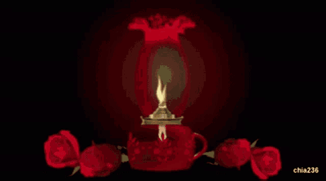 a red vase with a candle inside of it and red roses in the background
