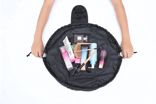 a person is holding a black bag filled with makeup and a bottle of perfume